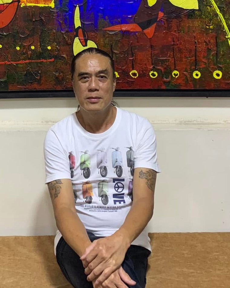Aye Ko seated in front of one of his paintings